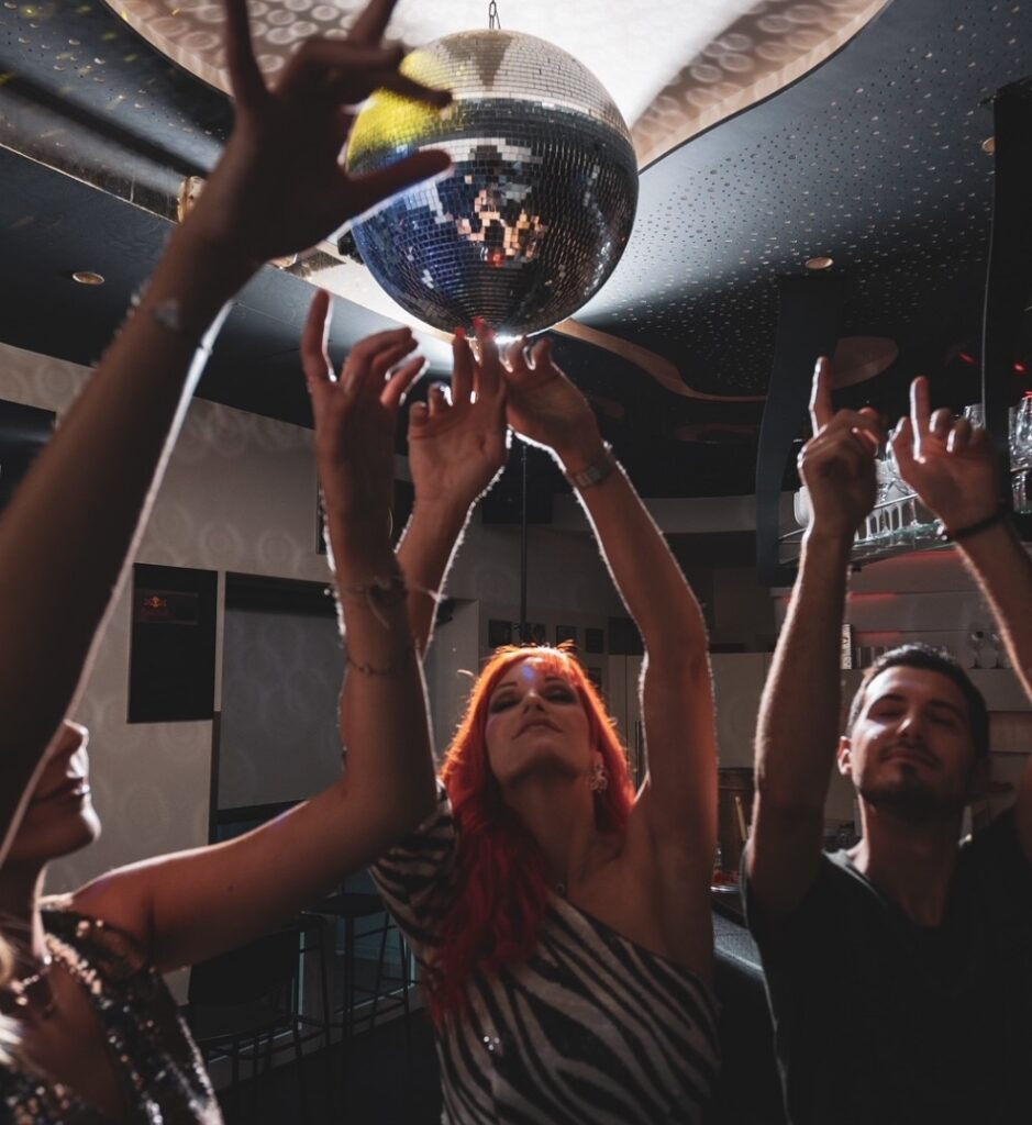 Drei Personen tanzen in einer Disco unter einer Discokugel ausgelassen.